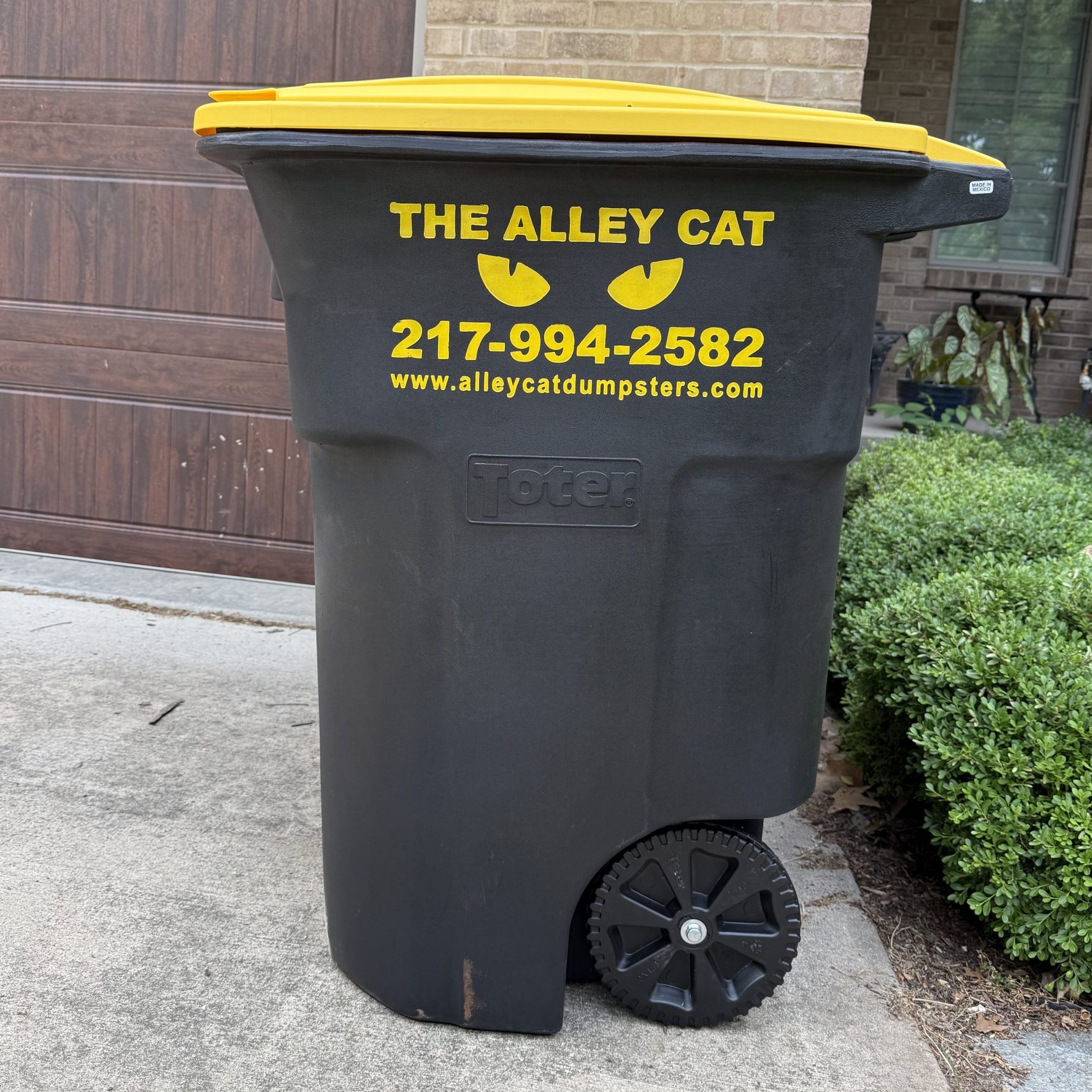 black and yellow trash bin that reads "The Alley Cat 217-994-2582 www.alleycatdumpsters.com"
